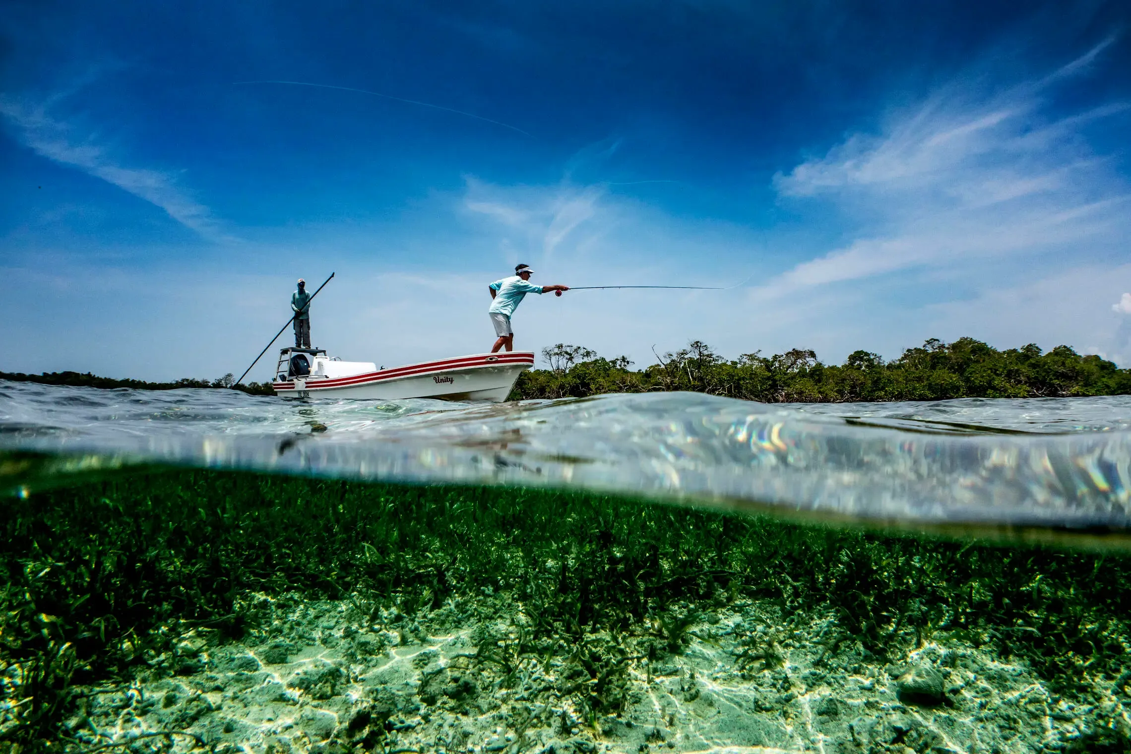 Angler on a fishing skiff over shallow flats in Belize, poling toward permit and bonefish territory near Ambergris Caye