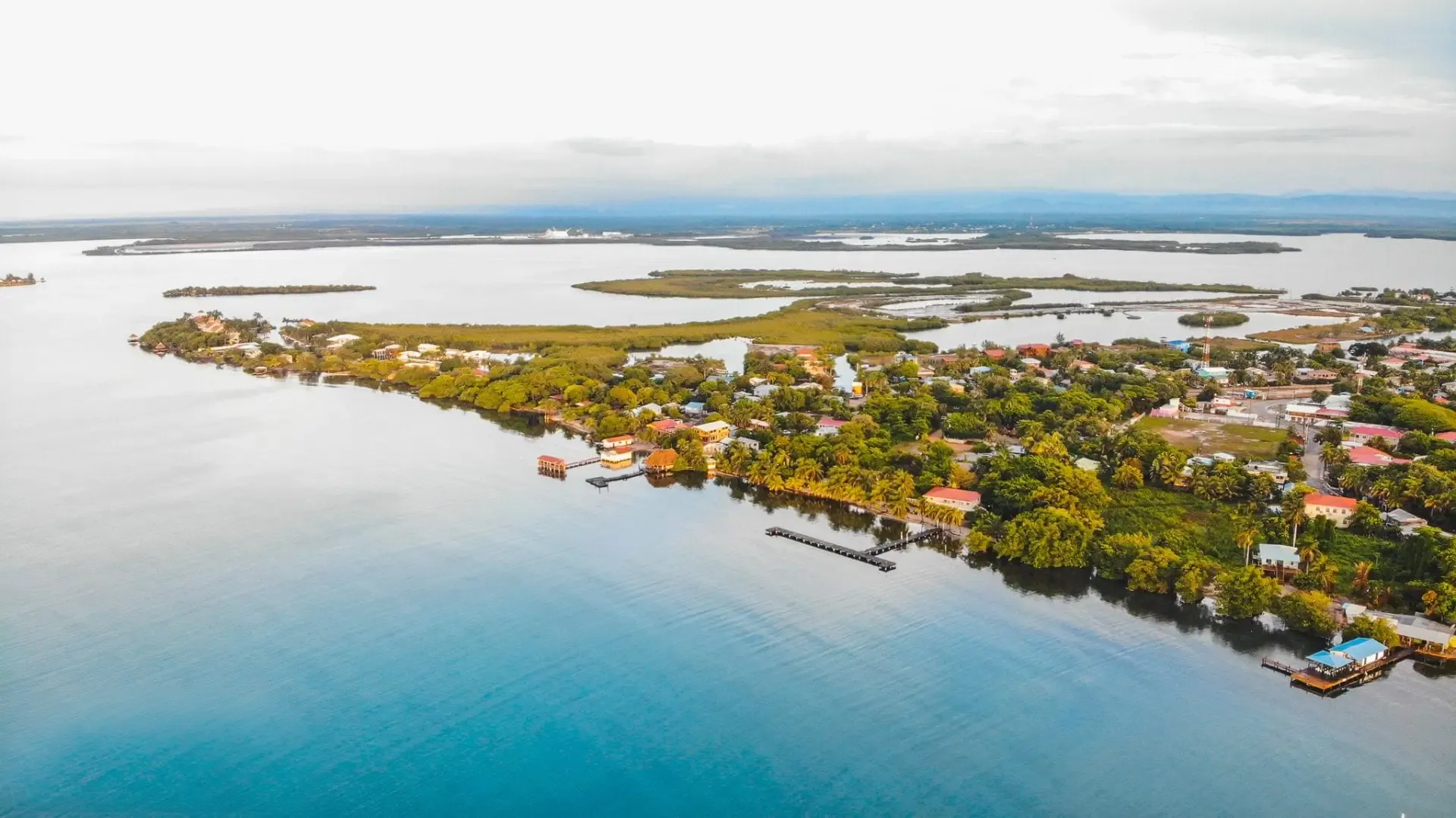 Aerial view of the Placencia Peninsula at golden hour — narrow strip of land between the Caribbean Sea and the Placencia Lagoon, warm amber light